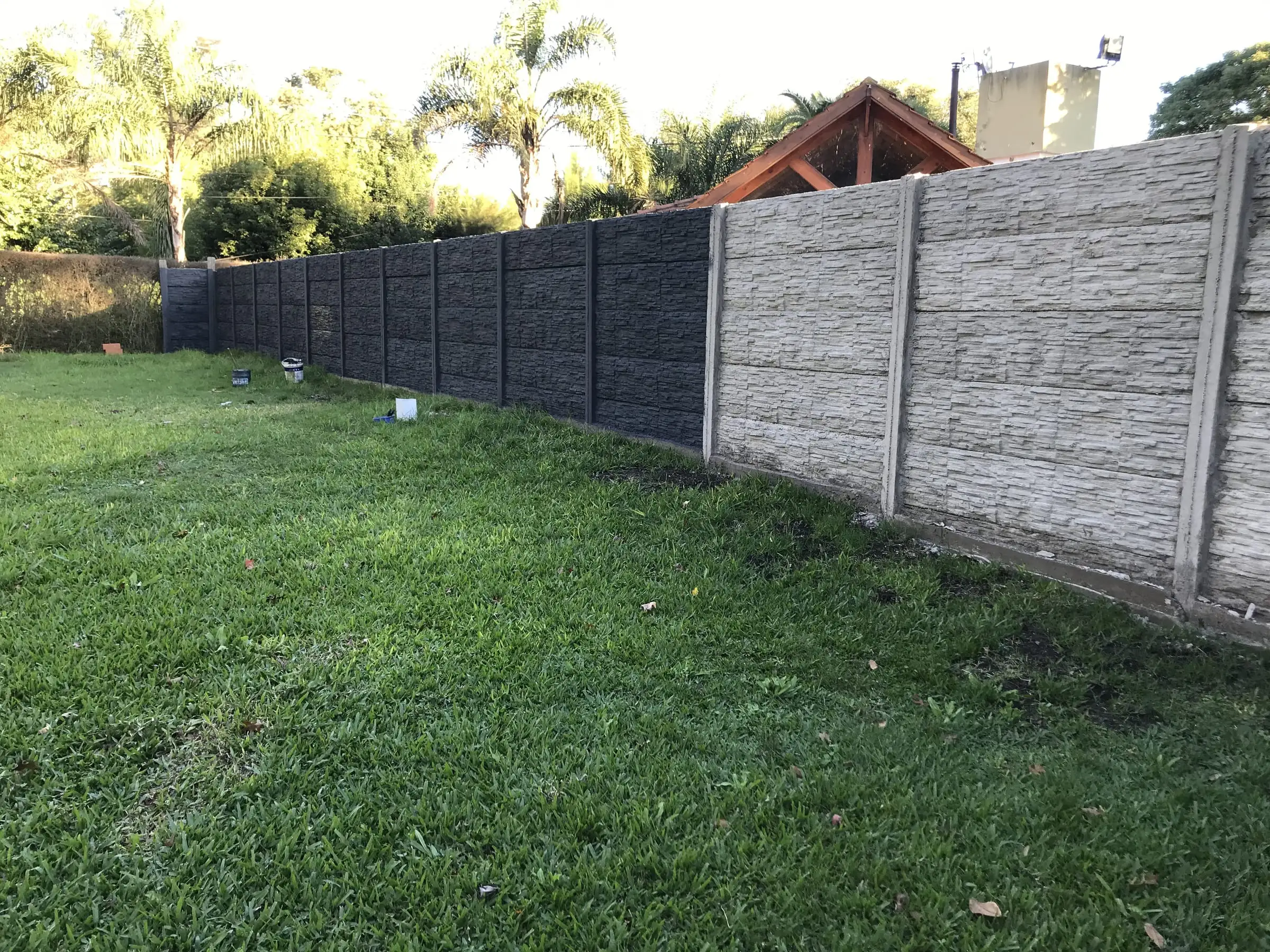 Cerco premoldeado texturado gris recién colocado sobre césped en una casa de zona norte